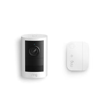 Ring indoor camera with black lens panel and speaker grille, shown beside a small white Ring hub on a plain white background.