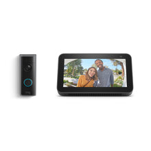Ring video doorbell next to a smart display showing two smiling visitors at a front door on a sunny day.
