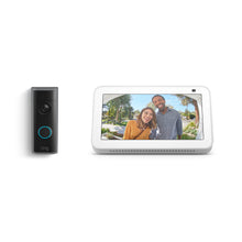 Black Ring doorbell next to a white smart display showing a wide-angle view of two smiling visitors at a front door.