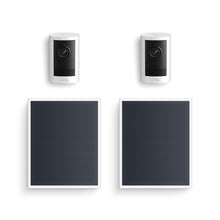 Two white Ring indoor/outdoor cameras paired with two rectangular black solar panels on a white background.