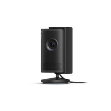 Black indoor security camera on a stand with power cable, single lens, perforated speaker grill, and small status light.