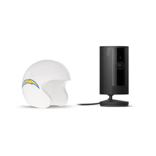 Black Ring indoor camera on a stand next to a white football helmet with a blue-and-yellow lightning bolt logo on a white background.