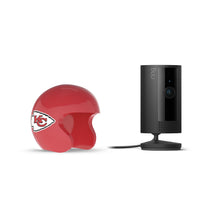 Black Ring indoor camera on a stand beside a red mini football helmet with the Kansas City Chiefs logo on a white background.