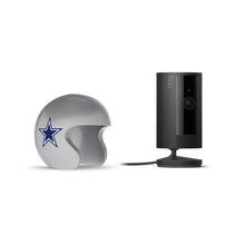 Black Ring indoor camera on a stand next to a silver football helmet with a blue star logo, against a white background.