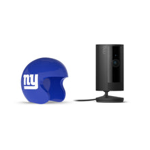 Black Ring indoor camera on a stand beside a blue mini football helmet with white “ny” logo on a white background.