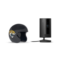 Black Ring indoor camera on a stand beside a glossy black helmet with a roaring jaguar logo, set against a white background.