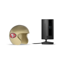 Black Ring indoor camera on a stand next to a gold mini football helmet with a red SF logo on a white background.