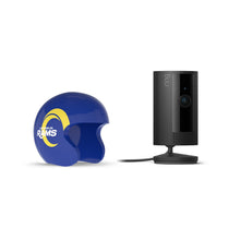 Black Ring indoor camera on a stand next to a blue Los Angeles Rams mini helmet cover with yellow horn logo on white background.