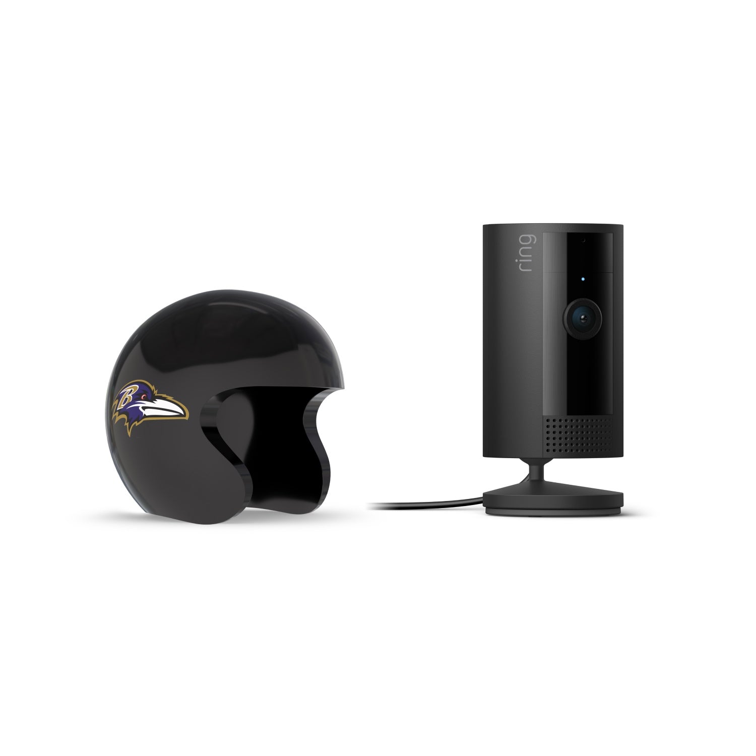 Black Ring indoor camera on a stand beside a glossy black football helmet with a purple-and-gold raven logo, set against a white background.