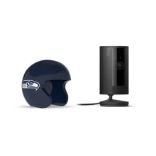 Black Ring indoor camera on a stand beside a navy mini football helmet with a hawk logo, set against a white background.