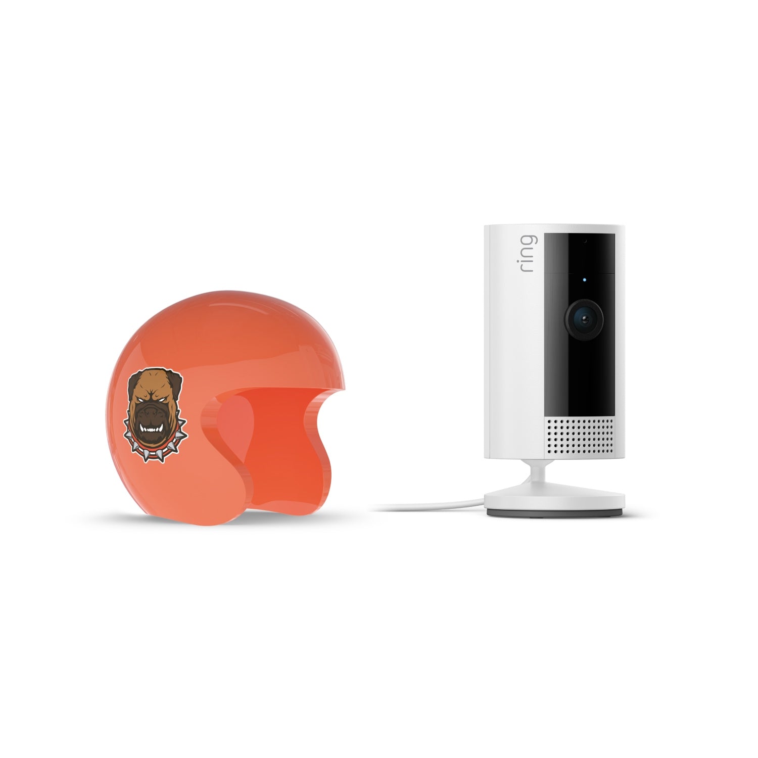 Orange helmet with a growling dog sticker next to a white Ring indoor camera on a stand with power cord, against a white background.