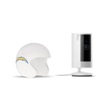 White Ring indoor camera on stand next to a white football helmet with a blue and yellow lightning bolt logo on a plain white background.