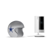 White Ring indoor camera on a stand next to a silver football helmet with a blue star logo, on a white background.