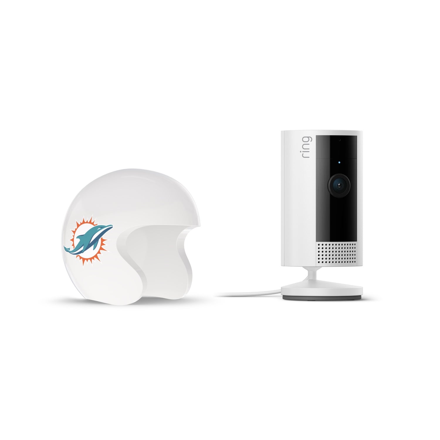 White Ring indoor camera on a stand next to a white mini football helmet with a teal dolphin logo on the side, set against a plain background.