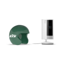 White Ring indoor camera on stand beside a glossy green Jets mini helmet on a white background.