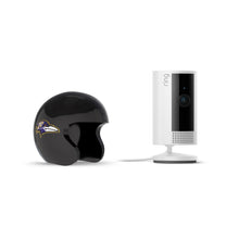 Black Baltimore Ravens mini helmet beside a white Ring indoor camera on a stand with power cable, set against a plain white background.