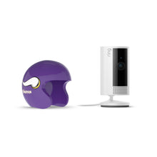 White Ring indoor camera on a stand next to a purple Minnesota Vikings mini helmet cover on a plain white background.