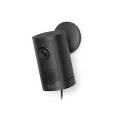 Black Ring stick-up outdoor camera mounted on a wall, showing lens, status light, speaker grill, and power cable.