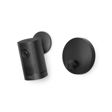 Black Ring outdoor security camera and round wall mount on a white background, showing lens, speaker grille, and logo.