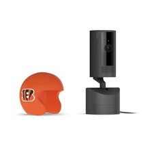 Black Ring indoor camera on a base next to an orange mini football helmet with a Bengals “B” logo, on a white background.