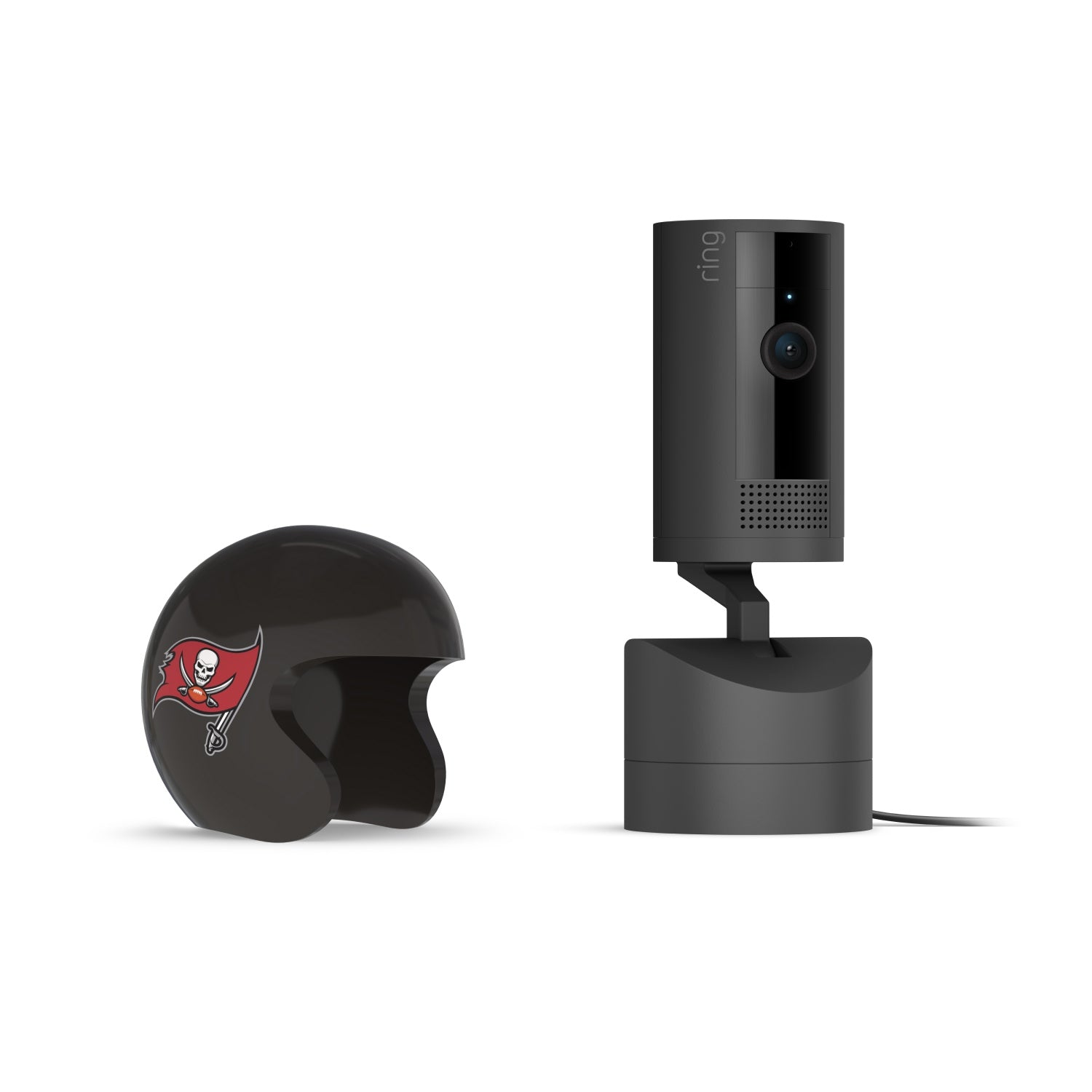 Black Ring indoor camera on a stand next to a small black helmet with a red Tampa Bay Buccaneers logo, on a white background.