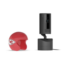 Black Ring indoor camera on a stand beside a small red Kansas City Chiefs helmet on a white background.