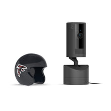 Black Ring indoor camera on a stand beside a small black helmet with the Atlanta Falcons logo, against a white background.