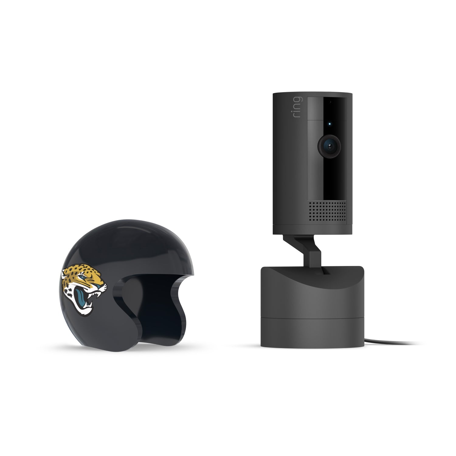Black Ring indoor camera on a stand beside a small black helmet with a jaguar logo, set against a white background.