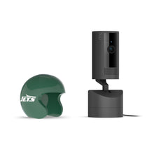Black Ring indoor camera on a charging base next to a small green New York Jets mini helmet on a white background.