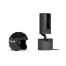 Black Ring indoor camera on a charging base beside a glossy black mini helmet with a purple raven logo on a white background.