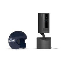 Black Ring indoor camera on stand with power cord, next to a dark blue mini football helmet featuring a hawk logo on white.