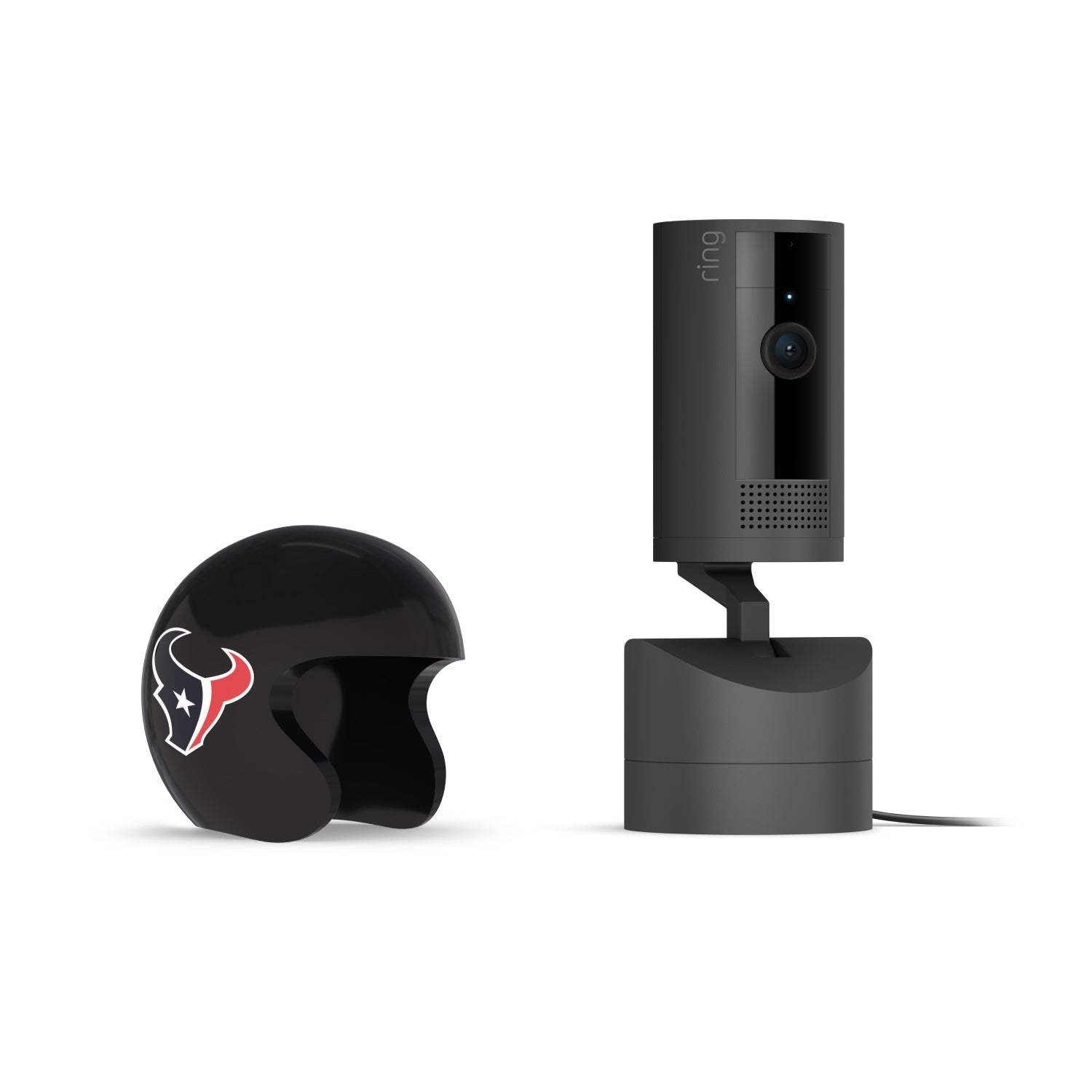 Black Ring indoor camera on a stand next to a small black helmet with the Houston Texans bull logo, on a white background.