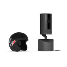 Black Ring indoor camera on a stand next to a small black helmet with the Houston Texans bull logo, on a white background.