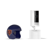White Ring indoor camera on a stand beside a navy mini football helmet with a roaring bear logo on a white background.
