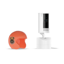 White Ring Pan-Tilt indoor camera on stand beside glossy orange open-face helmet with a fierce dog decal, on a white background.