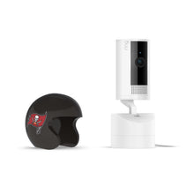 White Ring indoor camera on a white mount next to a small black football helmet with a red pirate flag logo on a plain white background.