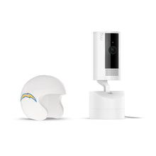 White Ring pan-tilt indoor camera on a stand next to a small white football helmet with a blue and yellow lightning bolt logo on the side.