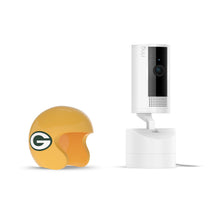 White Ring indoor camera on a stand next to a yellow Green Bay Packers mini helmet on a white background.