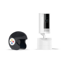 White Ring indoor camera on a stand beside a small black Pittsburgh Steelers helmet-shaped cover on a plain white background.