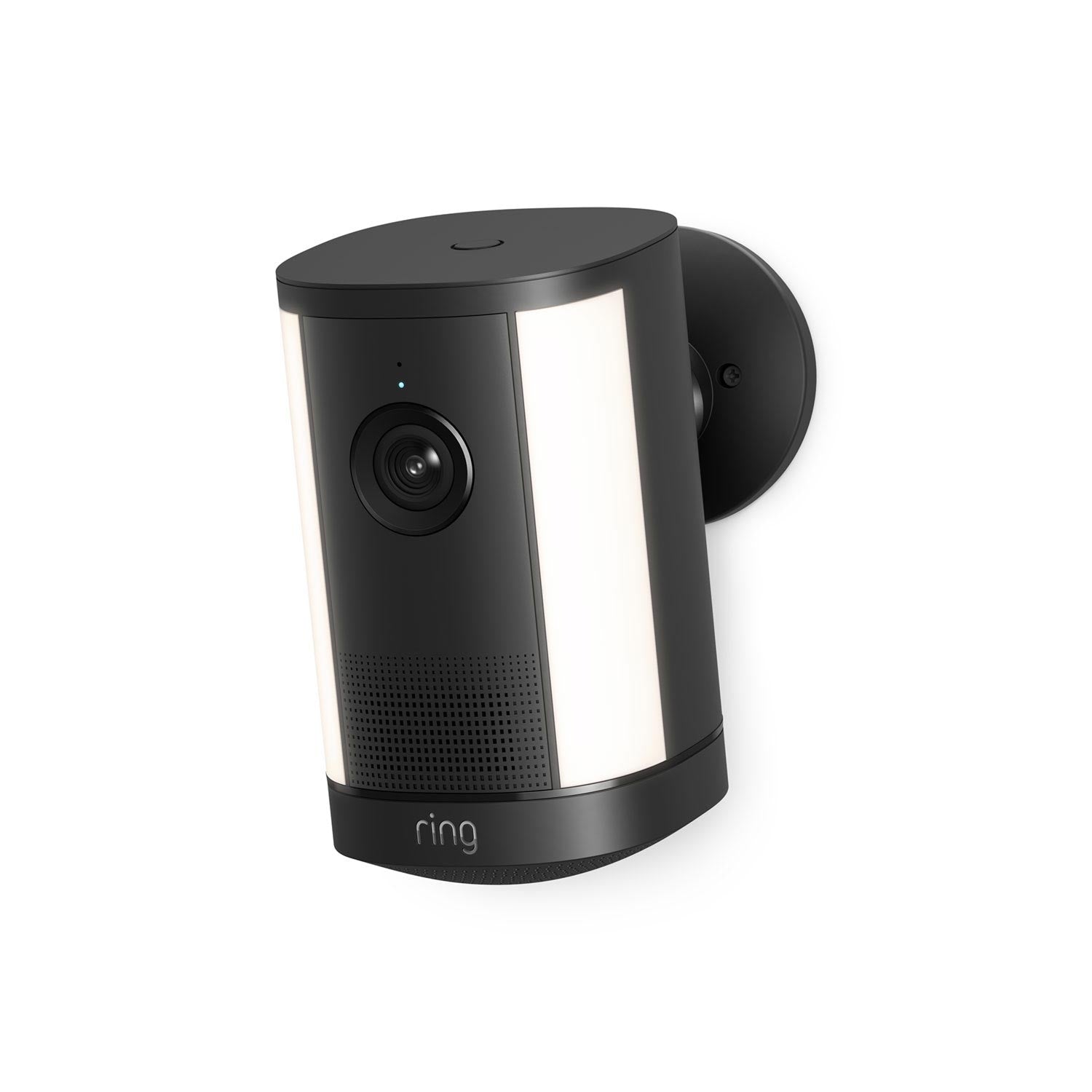 Wall-mounted black Ring camera with dual white light panels, wide lens, and speaker grille on a round base against a white background.