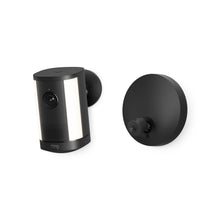 Black wall-mounted smart camera with dual side lights and speaker grille, shown with separate round mounting plate on white background.